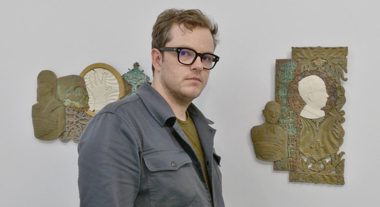 Peter Mammes standing before two of his relief works.
